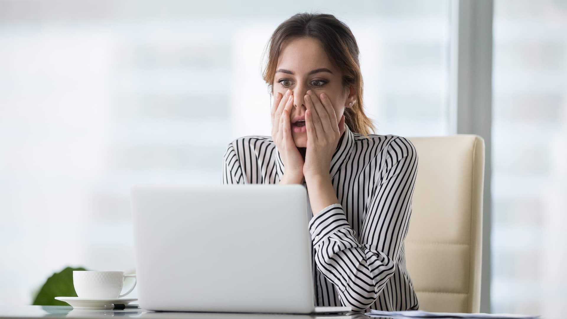 Woman looking shocked at her laptop, wanting to recall an email in Outlook