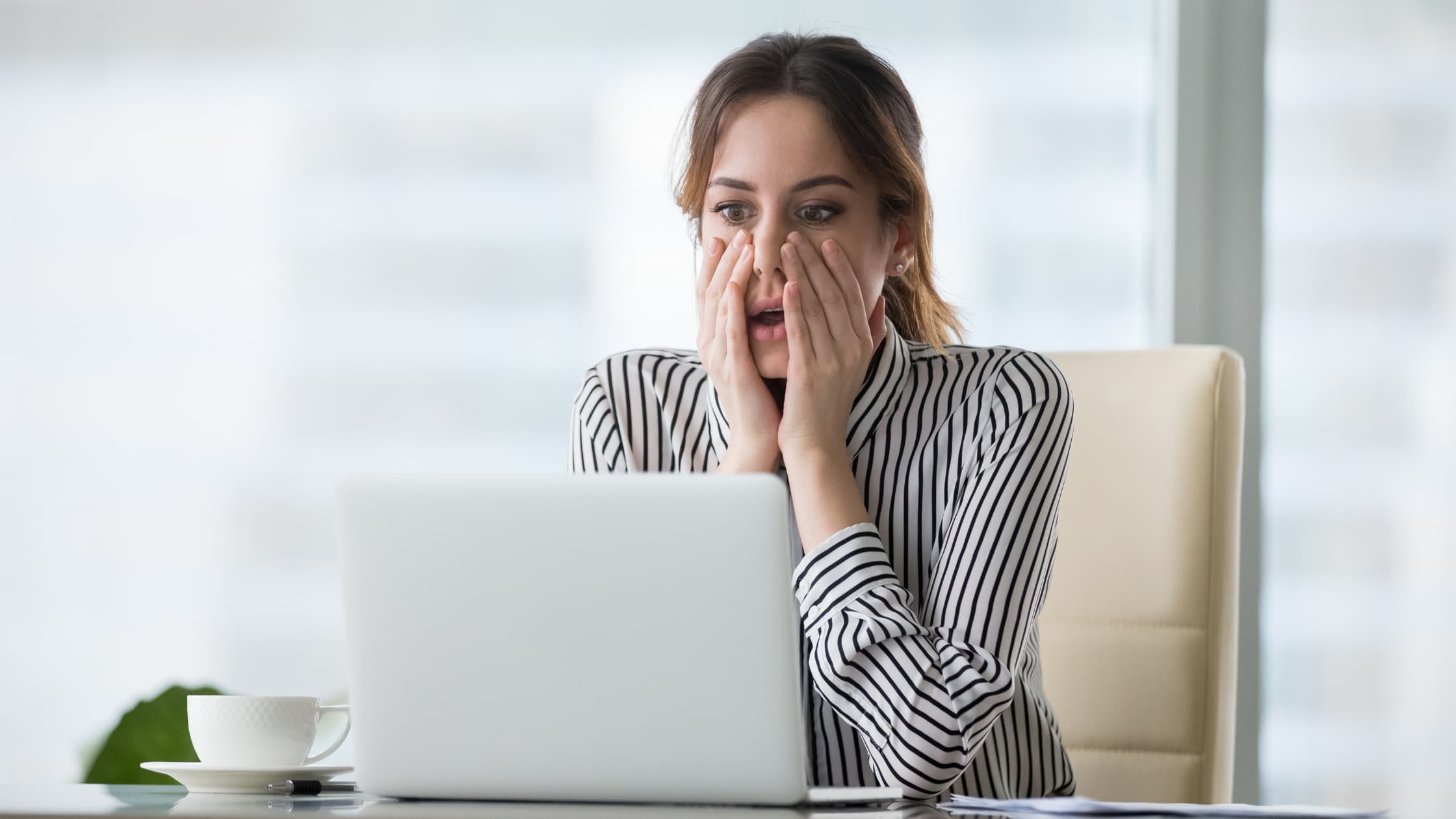 Woman looking shocked at her laptop, wanting to recall an email in Outlook