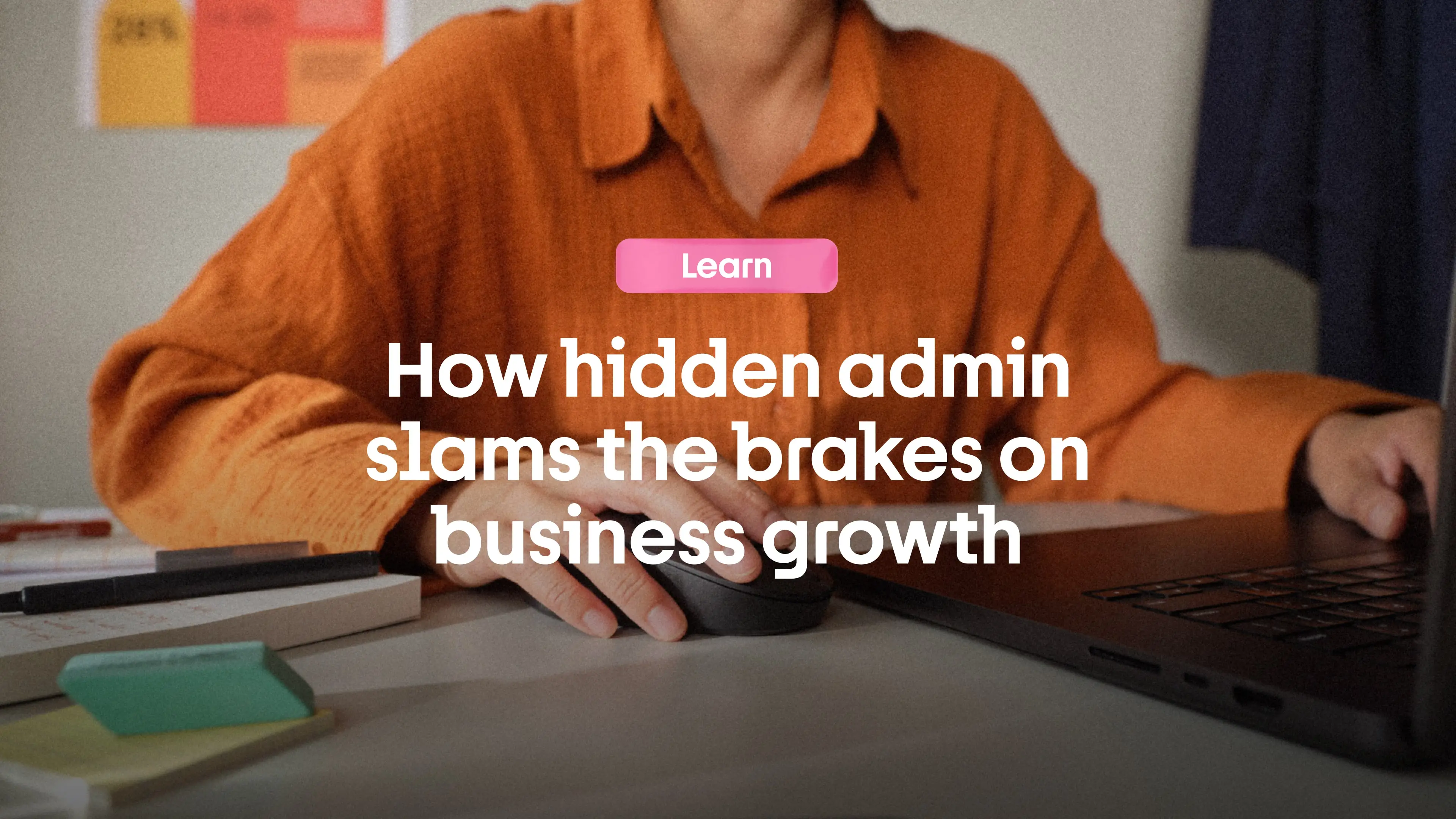Person in an orange shirt using a computer mouse and laptop with a message about hidden admin slowing business growth